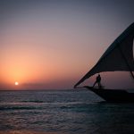 a person standing on a boat in the ocean at sunset