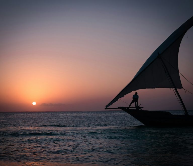 a person standing on a boat in the ocean at sunset